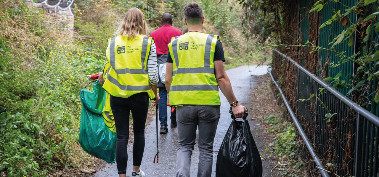 Two people walking in high-vis jackets with litterpicking gear